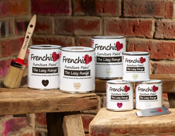 Stringers DIY Frenchic Furniture Paint cans on rustic wood with a paintbrush, against a brick wall background.