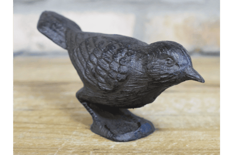 Cast iron bird sculpture with detailed feather texture, black finish, and standing on a wooden surface.
