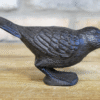 Cast iron bird sculpture with detailed feather texture, black finish, and standing on a small base on a wooden surface.