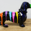 Decorative black dog figurine with colourful paint drips, on a wooden surface, for home decor or art display.