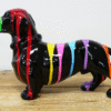 Colourful ceramic dachshund figurine with rainbow stripes on a wooden surface.