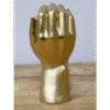 Decorative gold fist sculpture with a shiny finish, placed on a wooden surface against a plain background.
