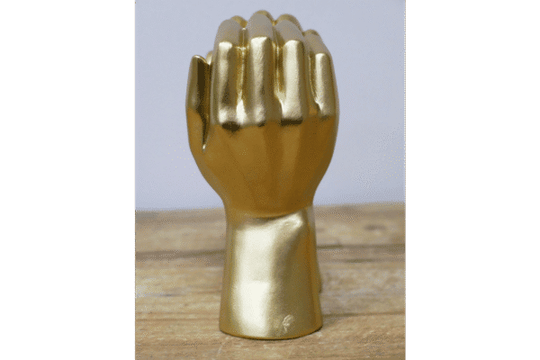 Decorative gold fist sculpture with a shiny finish, placed on a wooden surface against a plain background.