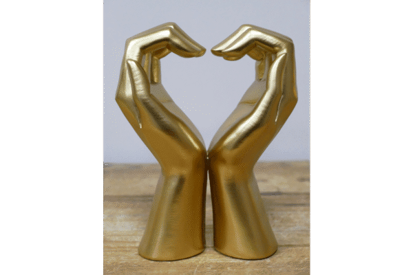Golden hand sculpture forming a heart shape, symbolising love and care, placed on a wooden surface.