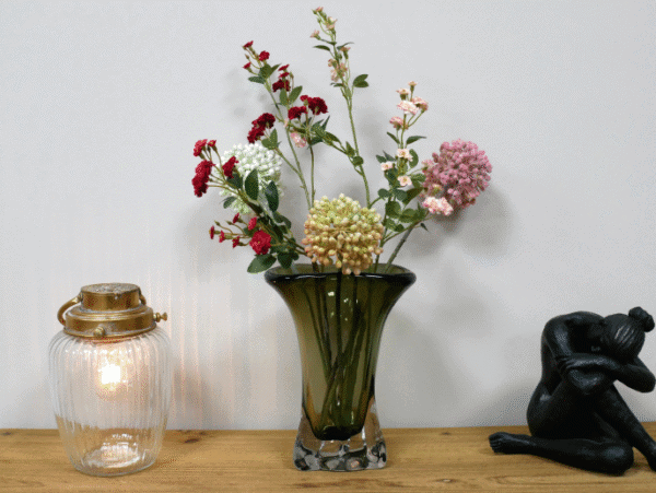 Elegant green glass vase with colourful flowers on a wooden surface, decorative items nearby.