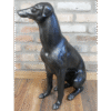 Decorative black sitting whippet sculpture made of metal or resin, positioned on a wooden floor against a brick wall.