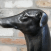 Close-up of a black dog sculpture with a smooth finish against a brick wall background.