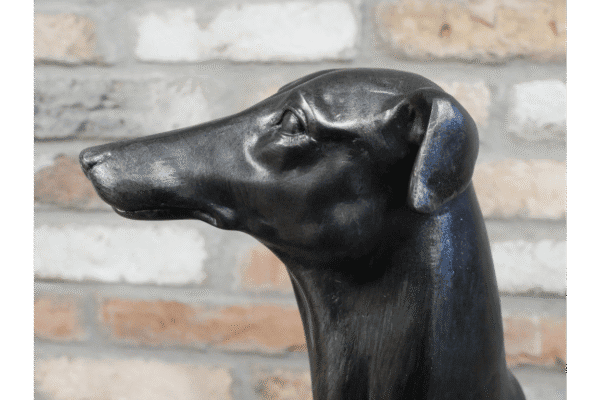 Close-up of a black dog sculpture with a smooth finish against a brick wall background.