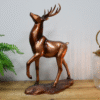 Decorative bronze stag ornament on a wooden surface with a green plant and glass lantern in the background.