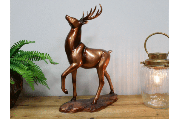 Decorative bronze stag ornament on a wooden surface with a green plant and glass lantern in the background.