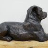 Bronze sculpture of a lying dog on a wooden surface, detailed and realistic in design.