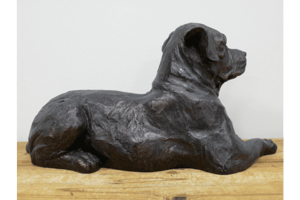 Bronze sculpture of a lying dog on a wooden surface, detailed and realistic in design.
