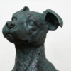 Bronze sculpture of a sitting dog with detailed features and a textured surface.