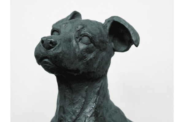 Bronze sculpture of a sitting dog with detailed features and a textured surface.
