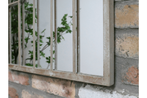 Close-up of a rustic arch mirror with a metal frame mounted on a brick wall, showcasing vintage industrial style decor.