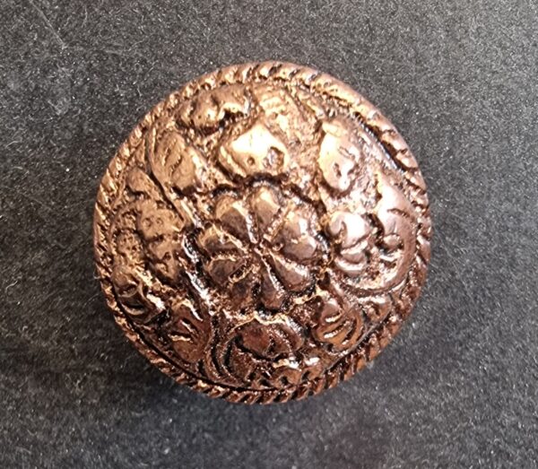 Close-up of a round metallic copper cabinet knob with intricate floral and geometric patterns, suitable for home decorating projects.
