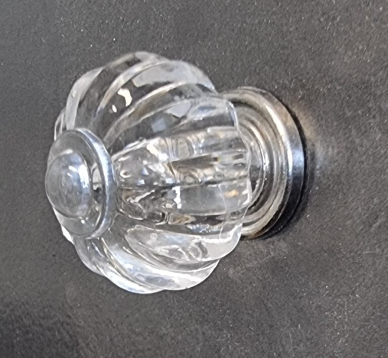 Close-up of a glass ribbed cabinet knob with a clear, textured design, mounted on a dark surface, ideal for home decorating projects.