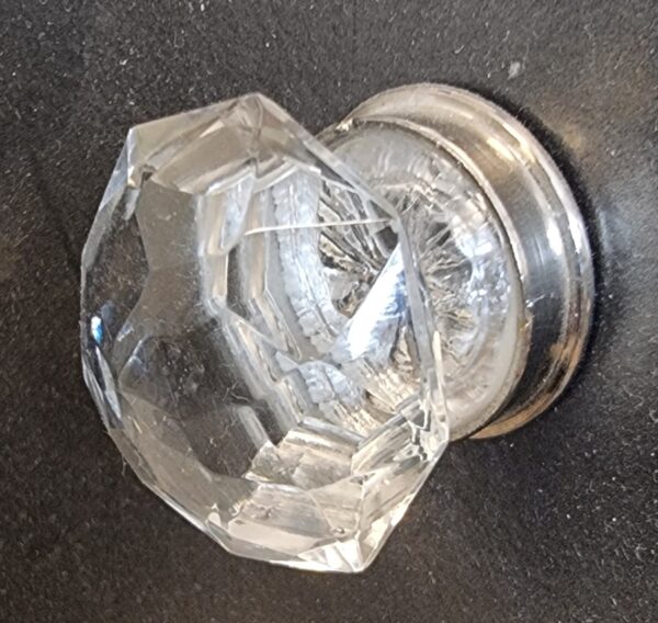Close-up of a cut glass globe with a reflective metallic base, used as a cabinet knob, on a dark surface.
