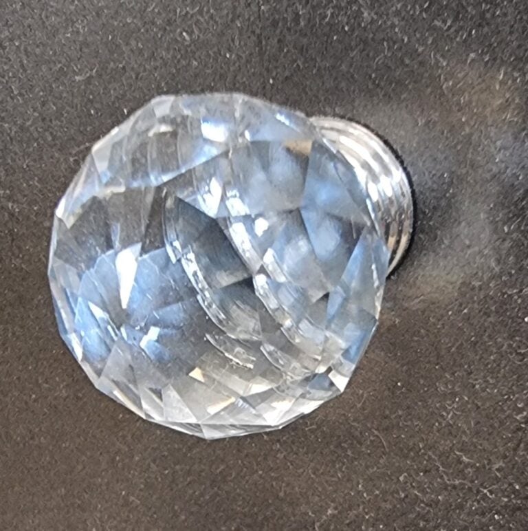 Close-up of a cut glass globe cabinet knob with intricate facets, mounted on a dark surface, showcasing its reflective and decorative qualities.