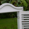 White shutter mirror with decorative top, set against green foliage, showcasing home decor and mirror design.