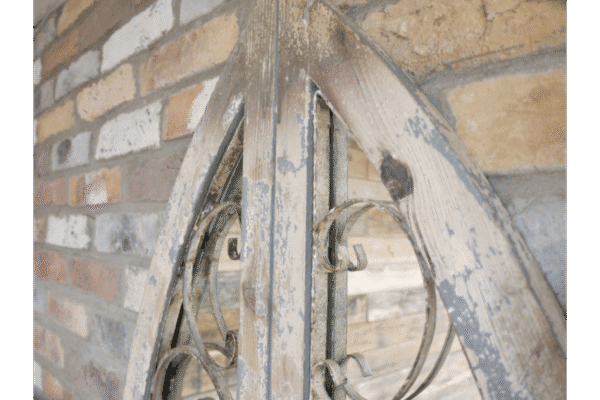 Close-up of a rustic, weathered wooden door with metal scrollwork, set against a brick wall, showcasing vintage charm and craftsmanship.