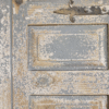 Close-up of a rustic, weathered wooden door with peeling paint and vintage metal hardware.