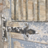 Close-up of a rustic metal gate with peeling paint and a latch, showcasing vintage industrial style.