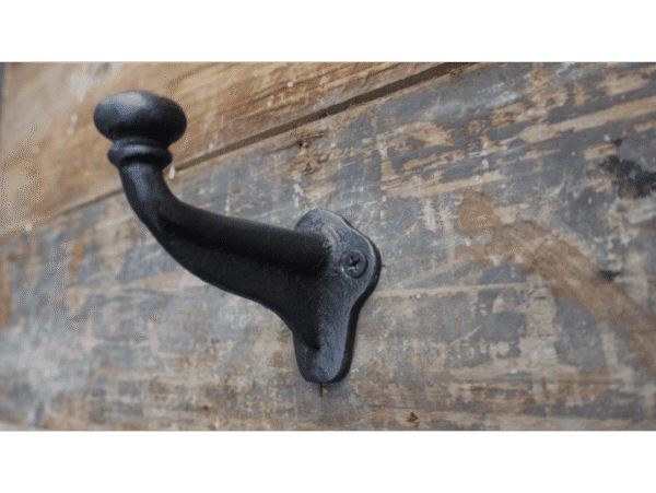 Industrial single coat hook made of black metal mounted on a weathered wooden wall.