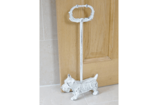 White metal door stop shaped like a Westie dog with a handle on top, placed on a tiled floor next to a wooden door.