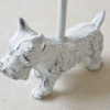 Decorative white dog-shaped door stop with a metal pole, designed as a Westie breed, placed on a tiled floor.