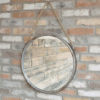 Industrial round metal and rope mirror hanging on a brick wall, suitable for home decorating.