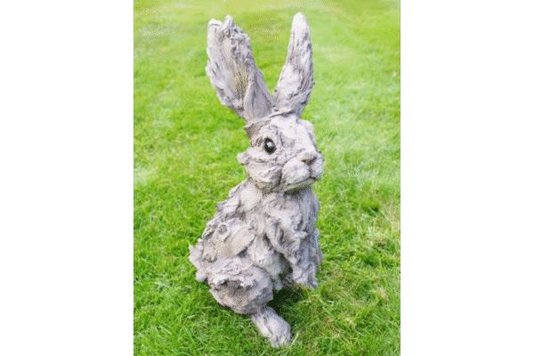 Large wooden rabbit sculpture with a textured, weathered finish, sitting on a grassy lawn, ideal for garden decor or outdoor decoration.