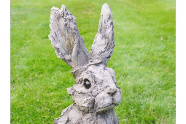 Large wooden rabbit sculpture with a textured, weathered finish, featuring tall ears and detailed facial features, set against a grassy background.