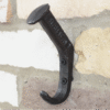 Railway pin coat hook mounted on a brick wall, black metal finish, sturdy and functional design.