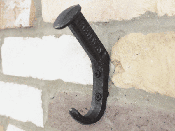 Railway pin coat hook mounted on a brick wall, black metal finish, sturdy and functional design.