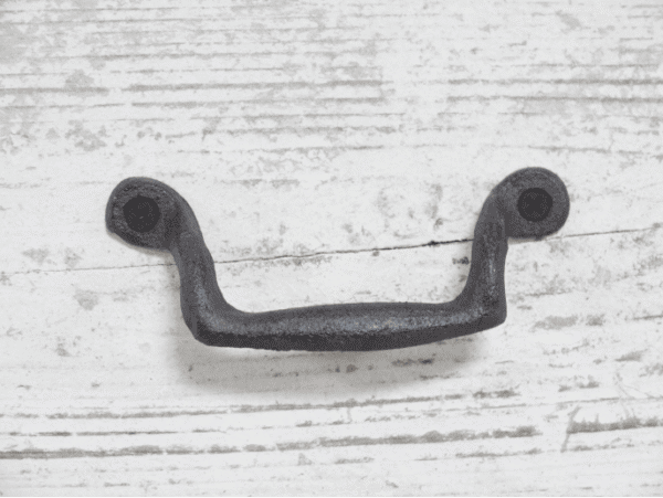 Wrought iron classic pull handle with black screws on a white wooden background, ideal for home decorating projects.