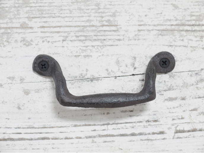 Wrought iron classic pull handle with black screws on a white wooden background, ideal for home decorating projects.