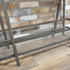 Industrial console table with metal frame and wire mesh shelf, set against a brick wall and wooden floor.