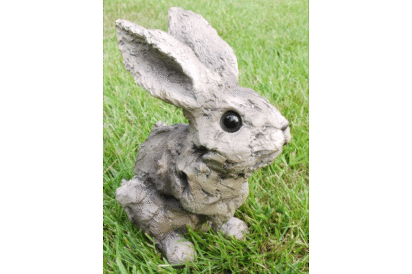 Decorative bunny sculpture with a wood effect finish, featuring large ears and black eyes, placed on a grassy surface.