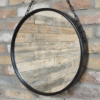 Round black mirror with chain hanging on a brick wall, ideal for home decor and interior design.