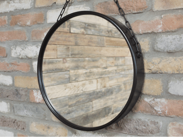 Round black mirror with chain hanging on a brick wall, ideal for home decor and interior design.