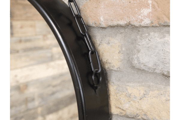 Close-up of a round black mirror with a chain hanging on a brick wall, showcasing modern home decor details.