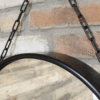 Close-up of a round black mirror with a chain hanging against a brick wall, showcasing modern home decor.