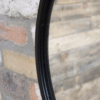 Close-up of a round black mirror with a chain, mounted on a textured brick wall, showcasing modern home decor style.