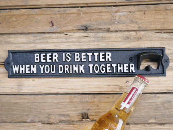 Decorative black sign with white text reading 'Beer is better when you drink together' on a wooden surface.