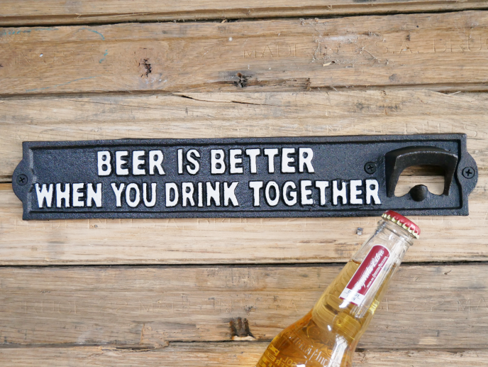 Decorative black sign with white text reading 'Beer is better when you drink together' on a wooden surface.