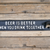 Decorative metal sign reading 'Beer is better when you drink together' on wooden background.