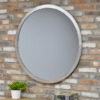 Industrial round silver mirror with a concrete frame hanging on a brick wall, with a small potted plant and books below.