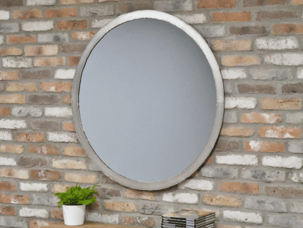 Industrial round silver mirror with a concrete frame hanging on a brick wall, reflecting a plain background.