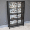 Industrial Safari Display Cabinet with glass doors and tropical-themed wallpaper background, ideal for home decor and display purposes.